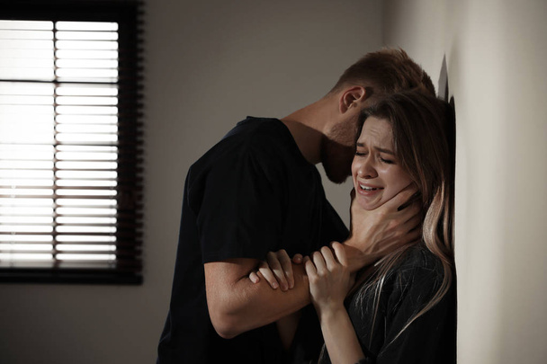 Man choking young woman indoors. Stop sexual assault - Zdjęcie, obraz