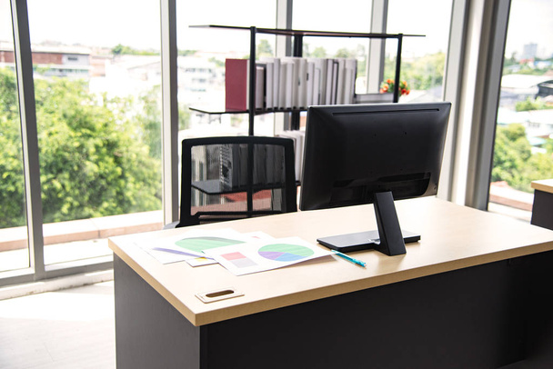 Modern kantoor interieur met tafel, computer, monitor, rapport en grote glazen raam rond de kamer zonder mensen - Foto, afbeelding
