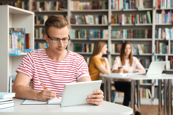 Jeune homme étudiant avec tablette à table à la bibliothèque. Espace pour le texte
 - Photo, image