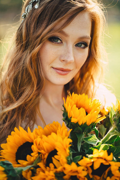 portrait of a young beautiful redhead woman with a bouquet of sunflowers in sunset light - Foto, afbeelding