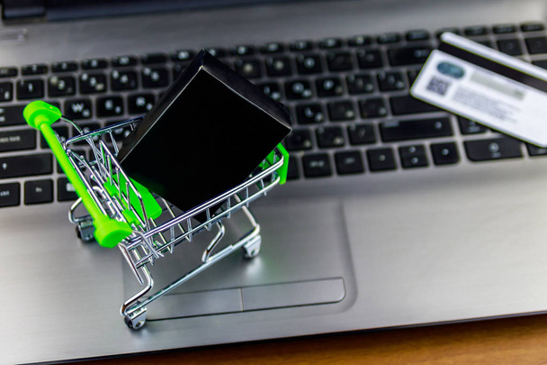 Online nákupní koncepce. Malý nákupní vozík s krabička a kreditní kartou na klávesnici přenosného počítače - Fotografie, Obrázek