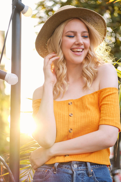 Portrait of cheerful blond girl in hat joyfully laughing standing on city street - Photo, Image