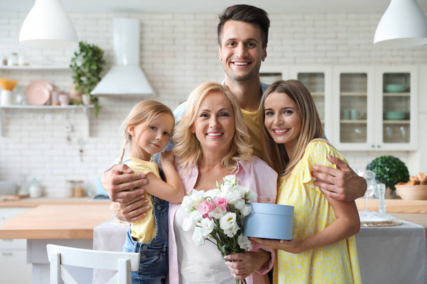 Portrait de famille heureuse avec bouquet et coffret cadeau dans la cuisine
 - Photo, image