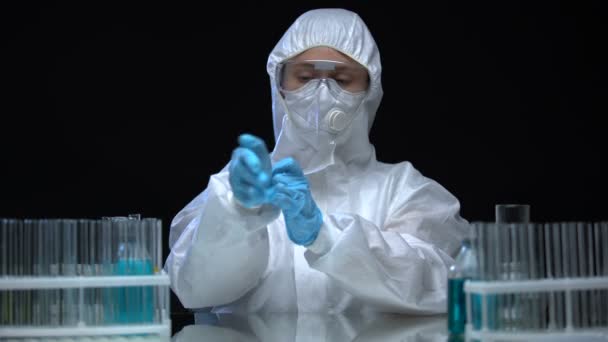 Lab worker in protective suit wearing rubber gloves, preparing for toxic work - Кадры, видео