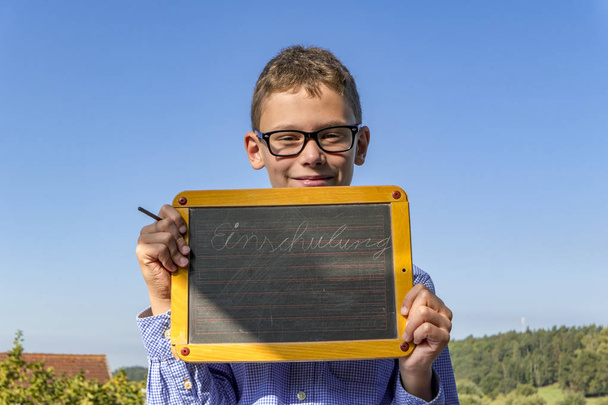 smart boy with glasses and blackboard on "school enrolment" insists in front of blue sky - Photo, Image