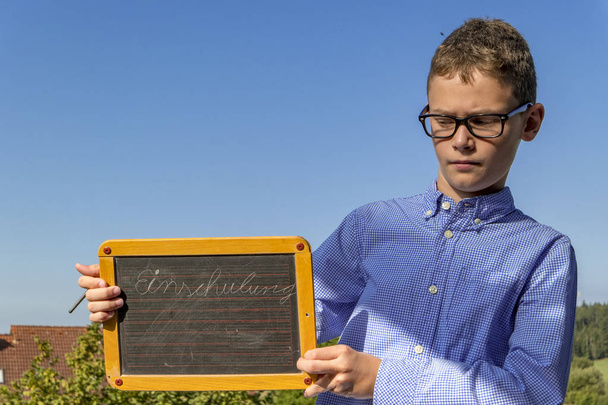 menino inteligente com óculos e quadro negro em "matrícula da escola" insiste na frente do céu azul
 - Foto, Imagem