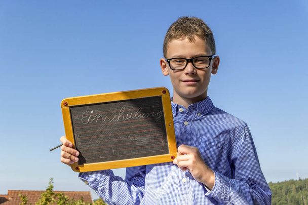Το αγόρι με τα γυαλιά και το μπλε πουκάμισο κρατά μια σανίδα με την επιγραφή "εγγραφή". - Φωτογραφία, εικόνα