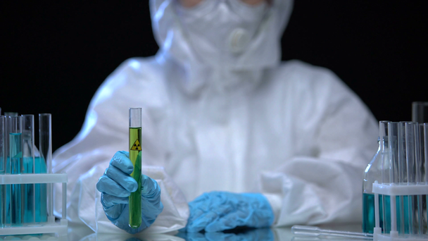 Toxic laboratory worker holding test tube with green ionizing radiation liquid - Filmati, video