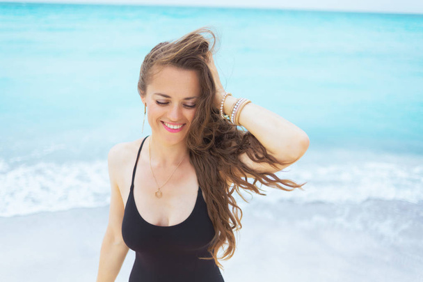 rilassato elegante donna di mezza età con lunghi capelli ricci in elegante costume da bagno nero su una spiaggia bianca
. - Foto, immagini