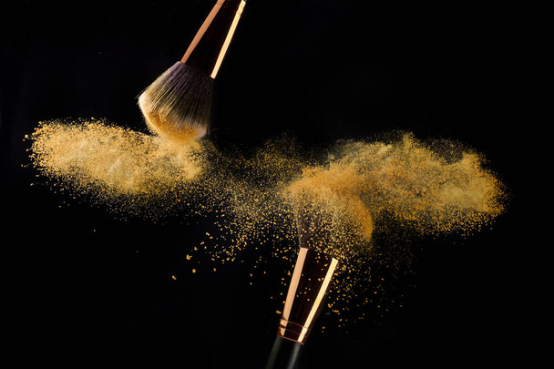 Cosmetic brush with golden powder spreading on black background - Zdjęcie, obraz