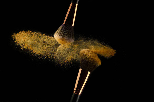 Cosmetic brush with golden powder spreading on black background - Фото, зображення
