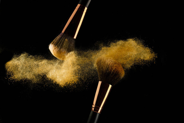 Cosmetic brush with golden powder spreading on black background - Valokuva, kuva