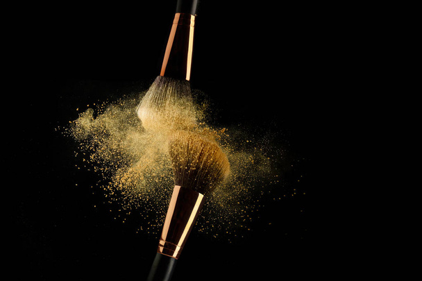 Cosmetic brush with golden powder spreading on black background - Photo, image