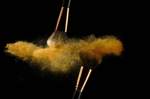Cosmetic brush with golden powder spreading on black background - Foto, afbeelding