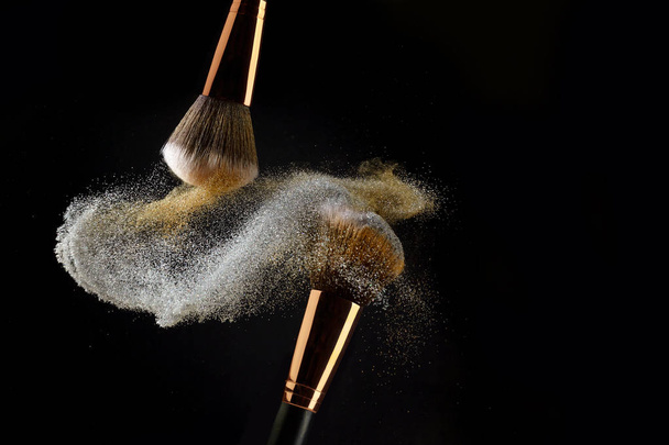Cosmetic brush with golden powder spreading on black background - Foto, imagen