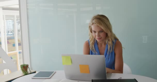 Vista frontal de un joven y sonriente negocio femenino caucásico creativo trabajando en una computadora portátil en una oficina
 - Metraje, vídeo