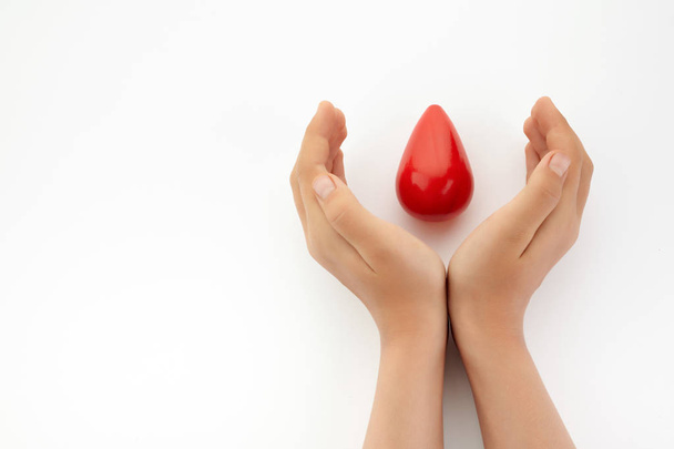 Two hands holding red blood drop on white background. Give blood. Donation concept. - Zdjęcie, obraz