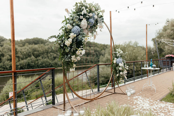 Arc de mariage avec des fleurs bleues et blanches debout sur la terrasse près de la rivière
 - Photo, image