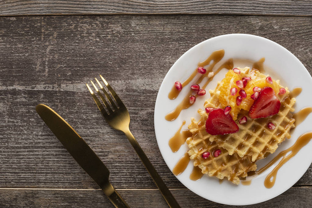 altın çatal ve bıçak ile beyaz bir arka plan üzerinde beyaz bir tabak üzerinde çilek ile waffle - Fotoğraf, Görsel