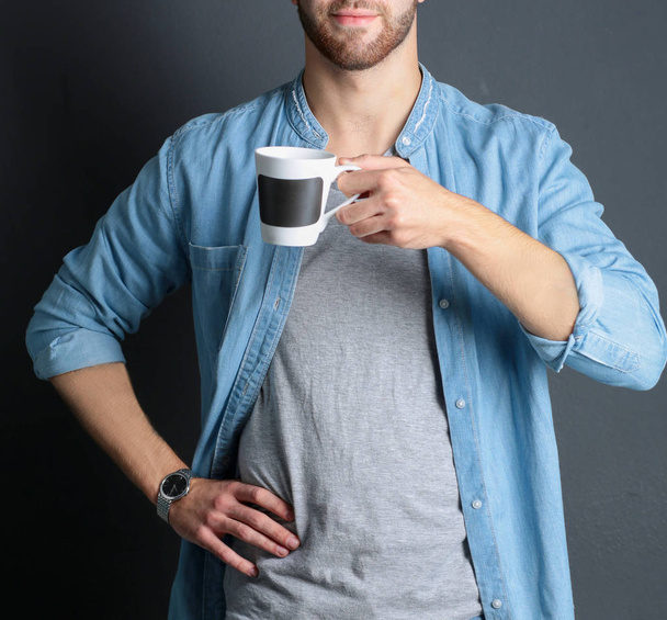 Portrait of a handsome young man standing and holding a cup of coffee in his hands - Foto, Imagem