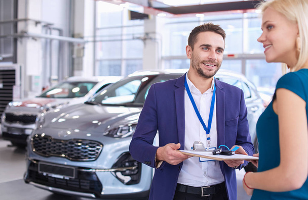 Car salesman sells a car to happy customer in car dealership and hands over the keys - Foto, Imagem