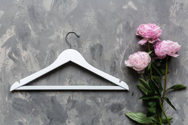 white wooden hanger and pink peony flowers on gray concrete background. Fashion feminine blog sale store promo design shopping concept. Flat lay, top view, mockup, overhead - 写真・画像