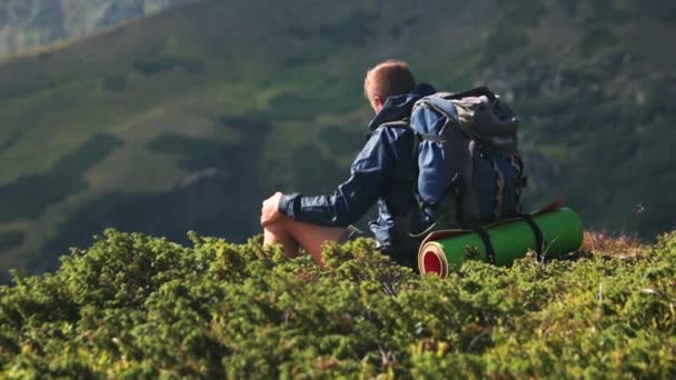 山の丘の上に座って、距離を見つめている若い観光客. - 映像、動画