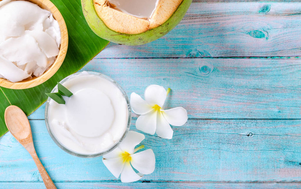 Młody budyń kokosowy podawany w szklanym kubku ozdobionym mięsem kokosowym wygląda przepysznie na liściach banana i pięknym, niebieskim drewnianym stole. Widok z góry. - Zdjęcie, obraz