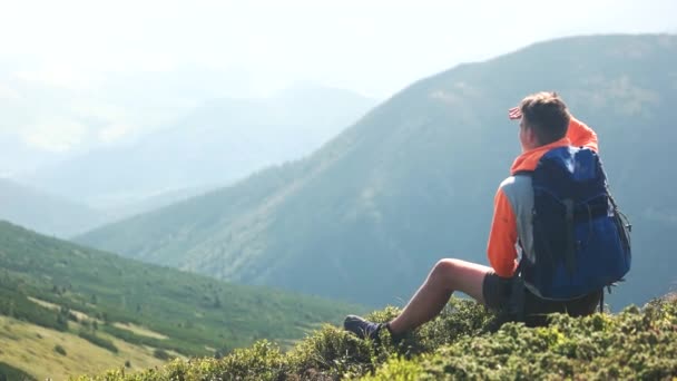 Ένας πεζοπόρος που κάθεται στο λόφο και απολαμβάνει τα βουνά. - Πλάνα, βίντεο