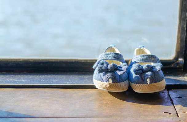 Buty dziecięce na drewnianej podłodze przy oknie ze światłem słonecznym. - Zdjęcie, obraz