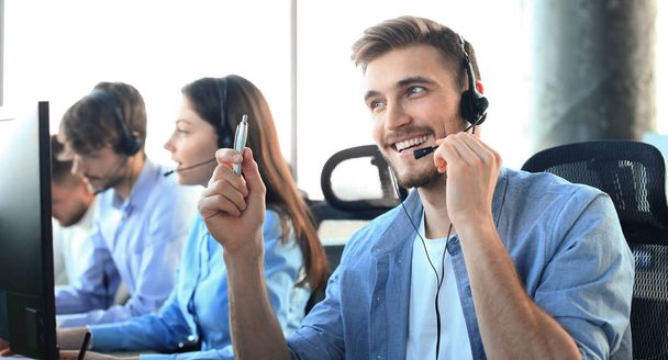 Portrait of call center worker accompanied by his team. Smiling customer support operator at work. - Photo, image