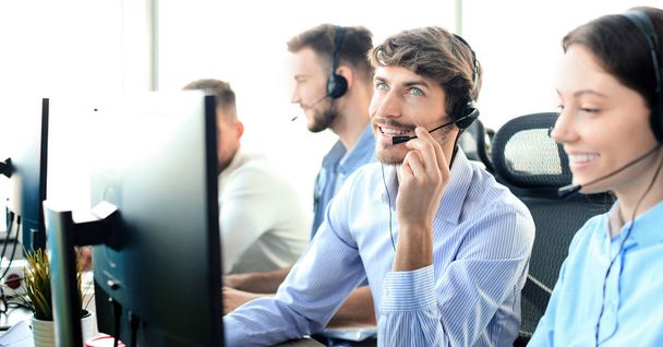 Portrait of call center worker accompanied by his team. Smiling customer support operator at work. - Fotó, kép