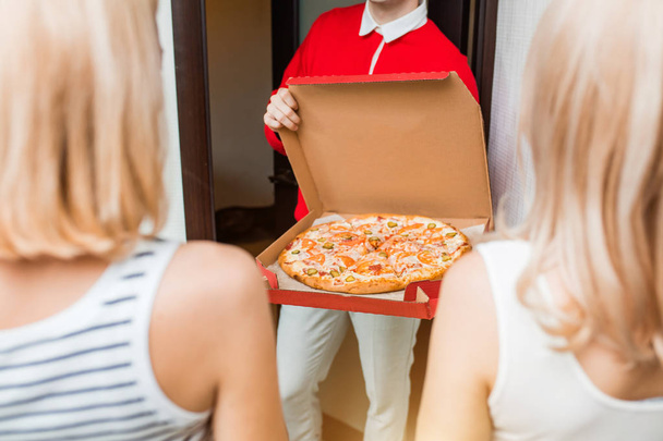 Two young caucasian woman receiving pizza from delivery man at home - Фото, зображення