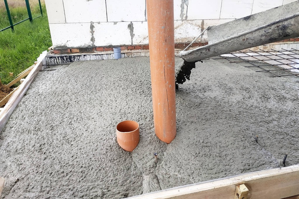 De betonmixer voedt cement door de goot om de betonnen plaat te gieten, rioolbuizen zijn zichtbaar. - Foto, afbeelding