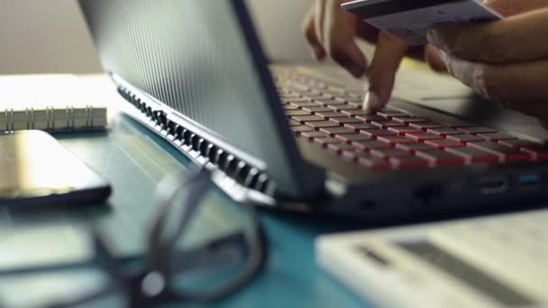 Handen van een man met een creditcard en laptop toetsenbord voor online betaling op het bureau thuis tijdens COVID-19 uitbraak situatie. Werk vanuit huis. - Video