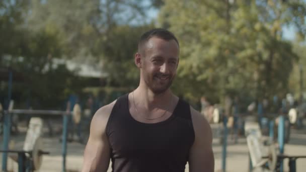 Smiling bodybuilder walking in outdoor gym - 映像、動画