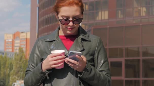 Young Woman Drinking Coffee on the Street, Typing Texting a Mobile Phone, While Walking in an Urban Setting. - Felvétel, videó