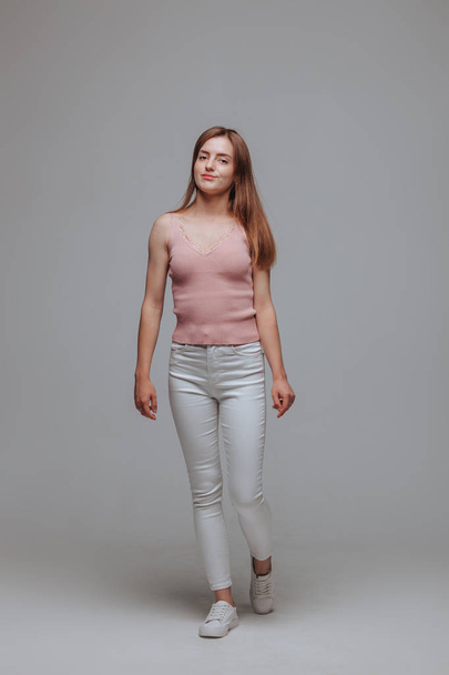 灰色の背景にピンクのTシャツと白いパンツの女の子 - 写真・画像