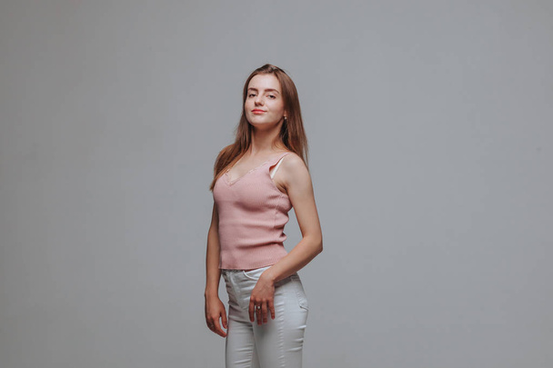 Κορίτσι με ροζ μπλουζάκι και λευκό παντελόνι σε γκρίζο φόντο - Φωτογραφία, εικόνα