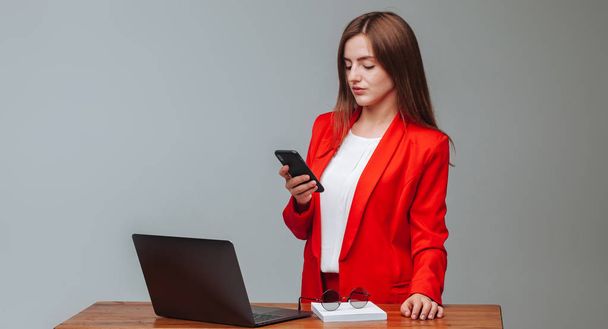 Девушка в красной куртке печатает сообщение по телефону в магазине
 - Фото, изображение