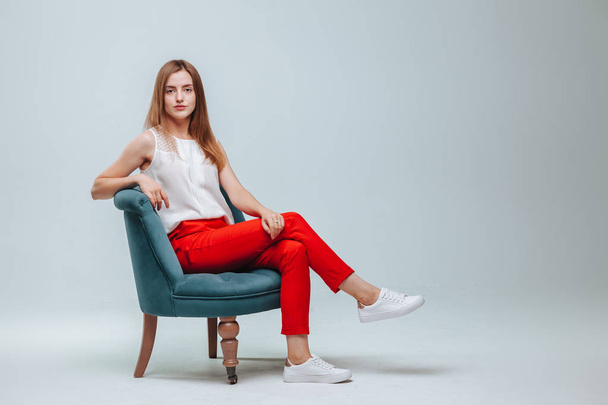 薄い灰色の背景に椅子に座っている赤いズボンの女の子 - 写真・画像