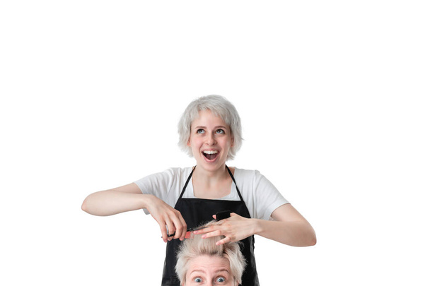 Jolie jeune coiffeur t-shirt blanc et tablier noir coupant les cheveux à une blonde avec coupe de cheveux courte. isolé sur fond blanc. Le client si un peu nerveux au sujet du résultat
. - Photo, image