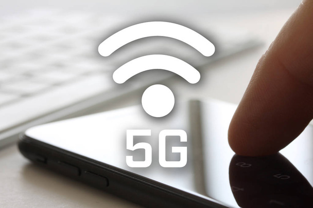 Concept de réseau 5G avec doigt toucher smartphone avec écran et clavier en arrière-plan. Symbole Internet sans fil devant l'écran
. - Photo, image