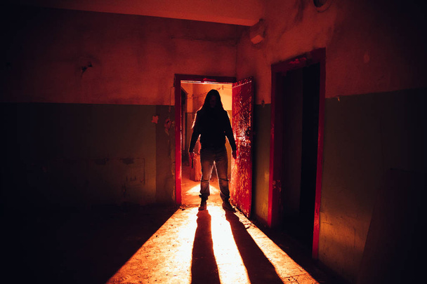 Silueta espeluznante con cuchillo en el oscuro abandono iluminado rojo
 - Foto, imagen