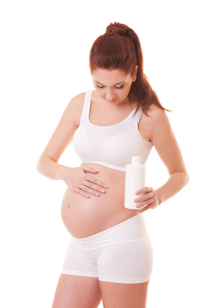 Pretty pregnant woman applying anti stretch marks cream on her body. Isolated on white. Care about skin at pregnancy period. - Φωτογραφία, εικόνα