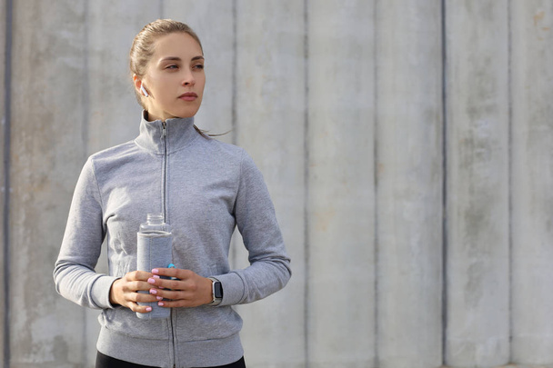 Schöne Läuferin steht draußen und hält Wasserflasche in der Hand. Fitness-Frau legt nach Lauftraining eine Pause ein - Foto, Bild