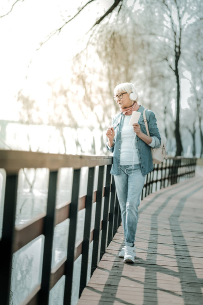 Peaceful grey-haired woman in earphone walking down the park - Foto, Imagen