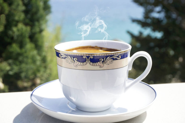 Filiżanka gorącej kawy na tarasie z niewyraźne morze i drzew w tle - Zdjęcie, obraz
