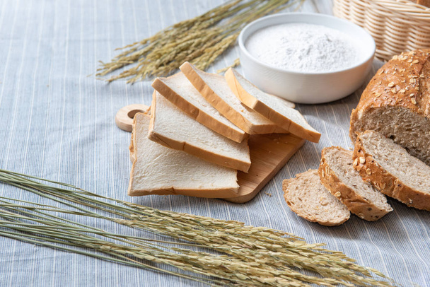 Schuif wit brood, volkoren tarwe met volkoren brood en witte klap meel op licht blauwe vloer met wat verse tarwe. - Foto, afbeelding