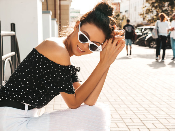 Beautiful smiling model dressed in elegant summer clothes.Sexy carefree girl sitting in the street background.Trendy modern businesswoman in sunglasses having fun - Foto, afbeelding